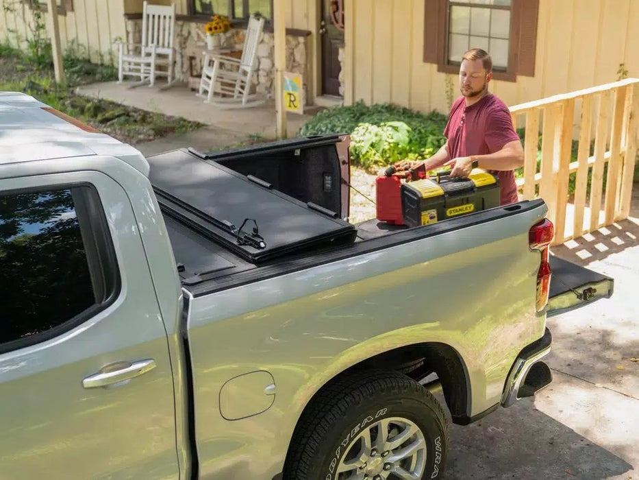 A man stands beside a truck with a toolbox, demonstrating the BAKFlip MX4 Tonneau Cover on the truck bed.