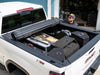 A man sits in the back of a truck with a toolbox, showcasing the BAK Revolver X4S Tonneau Cover above him.